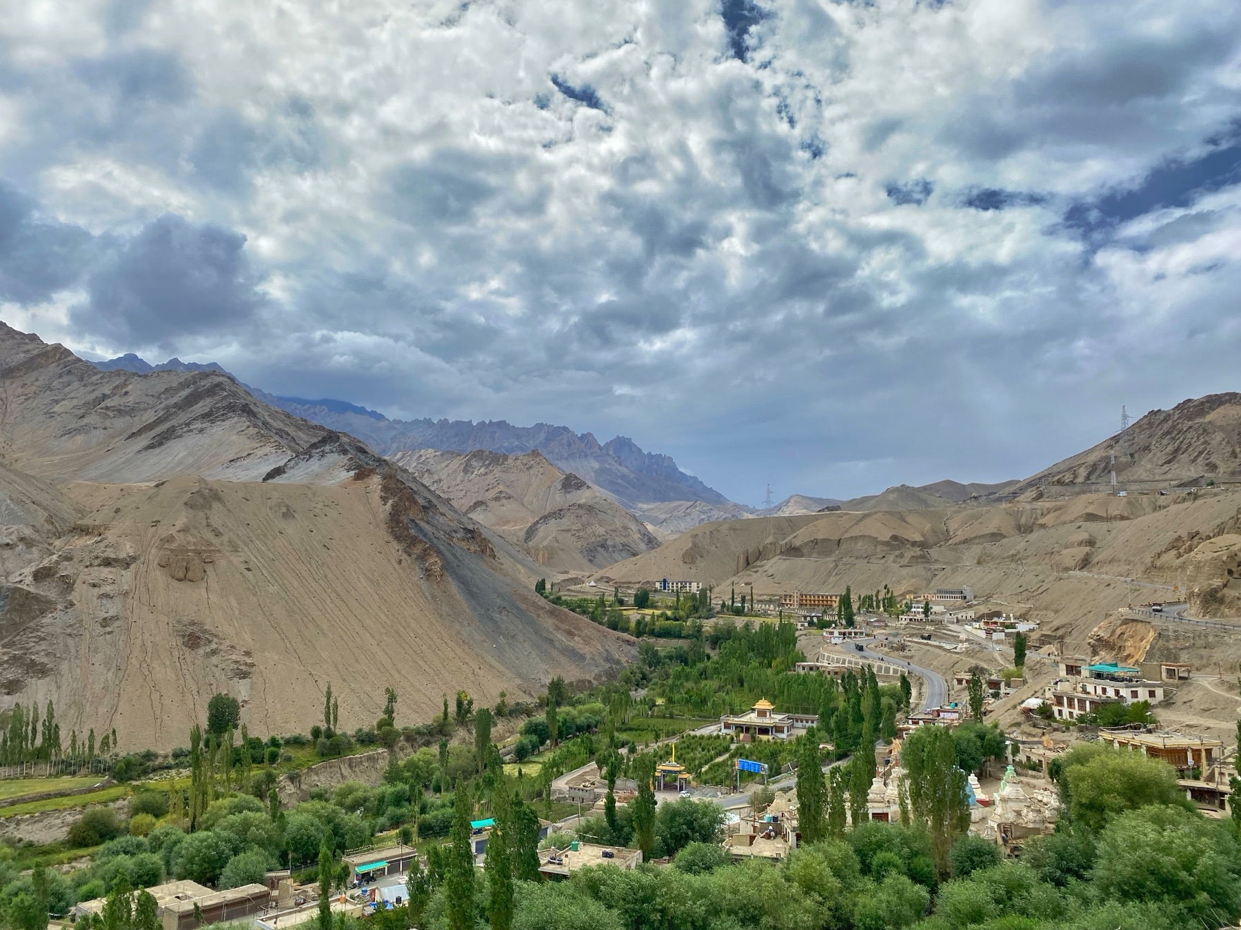 A green valley set among the dry mountains of Ladakh, India, under a dramatic cloudy sky