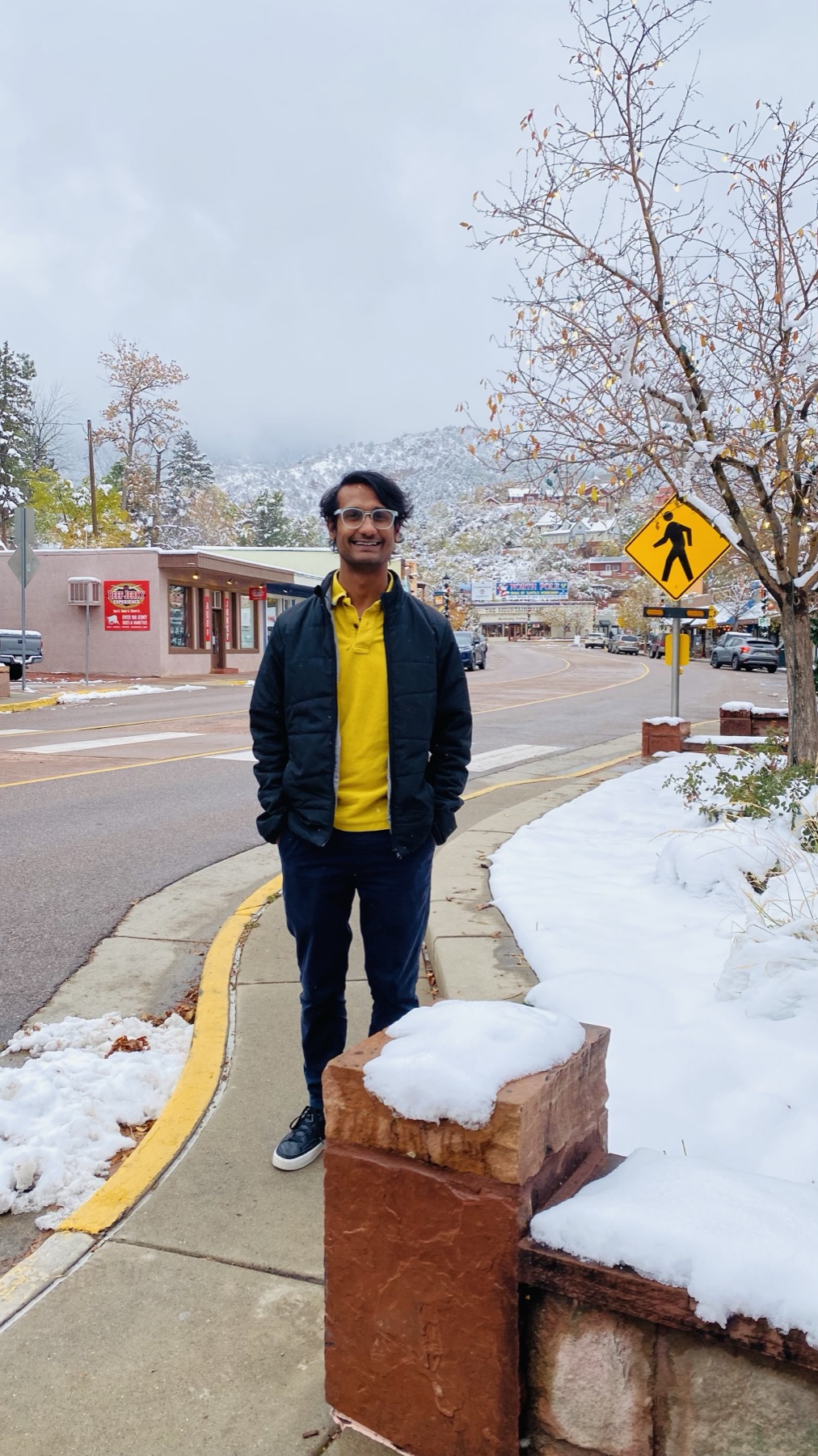 A snowy small-town street after an early snowfall, framed by mountains in the background